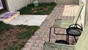 A patio area with hexagonal paving, two green metal chairs, a white door, and a 'Please clean up after your dog' sign.