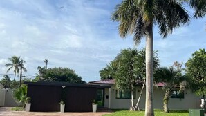 A residential property with a paved driveway, a covered outdoor area, and palm trees.