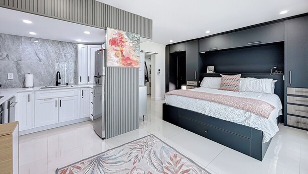A modern bedroom with a large bed, a built-in wardrobe, and a kitchen area with a marble backsplash.
