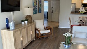 Un salon comprenant un téléviseur, un meuble, un canapé et une table à manger agrémentée d’un vase de fleurs.