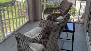 Un balcon abrité, doté de fauteuils en osier et d’une petite table, qui offre une vue sur un quartier résidentiel avec ses maisons et ses arbres.