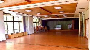 A spacious hall with wooden flooring, large windows, and a stage area with chairs and a laptop. - kogikusou (Kikugawa)