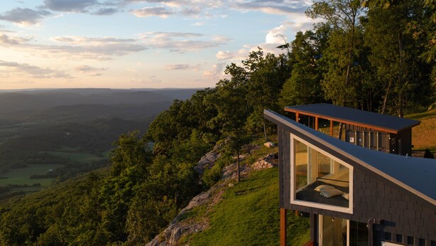 A modern house with a glass balcony overlooking a forested valley.