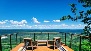 A wooden deck with two wicker chairs and a table, overlooking a lush valley.
