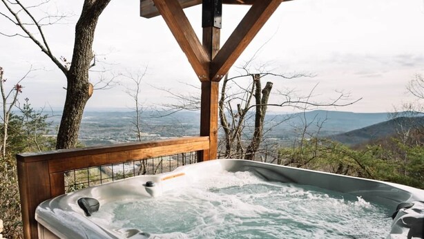 A hot tub with a wooden deck and a view of the mountains.
