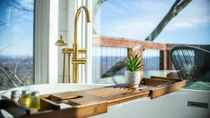 A modern bathroom with a white sink, gold fixtures, and a wooden tray.