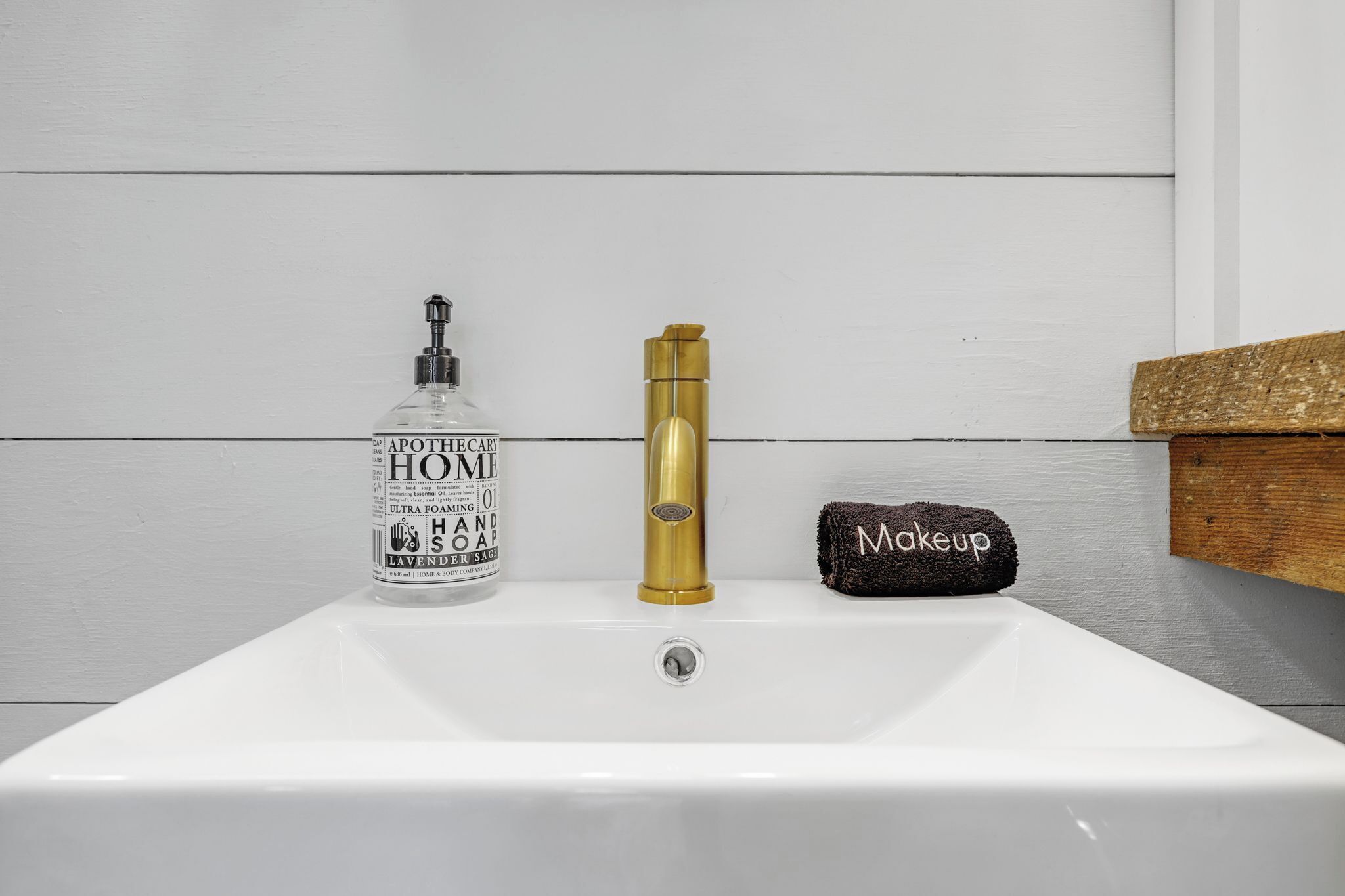 Kylpyhuoneen pesuallas, jonka vieressä on pullo Apothecary Home -merkkistä, runsaasti vaahtoavaa käsisaippuaa ja kultainen hana.