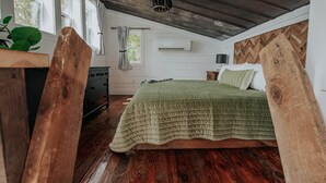 A bedroom with a wooden headboard, a green bedspread, a wooden dresser, and a window with curtains. - The Artistree House A Treehouse in Rising Fawn (Rising Fawn)
