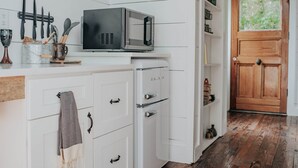 A kitchen with white cabinets, a microwave, and a wooden door. - The Artistree House A Treehouse in Rising Fawn (Rising Fawn)