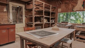 A rustic wooden room with a large window, shelves with pottery, and a table with a paper. - The Artistree House A Treehouse in Rising Fawn (Rising Fawn)