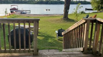 Relax on the lakeside deck with a grill, chairs, and a table, surrounded by a tranquil lake and lush greenery.