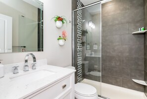 Un baño moderno con un tocador blanco, cabina de ducha con mampara de vidrio y dos macetas colgantes con flores.