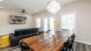 A dining area with a wooden table, black chairs, a chandelier, a black leather couch, and a painting on the wall. - Highlands Lookout-3BR 3.5BA-Walk to Tons +Parking (Louisville)