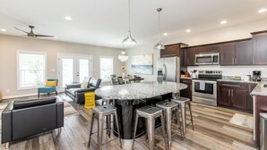 A modern kitchen with a central island, stainless steel appliances, and a dining area with a black leather sofa and yellow ottoman. - Highlands Lookout-3BR 3.5BA-Walk to Tons +Parking (Louisville)