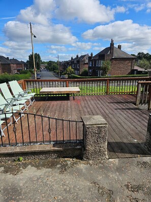 A wooden deck with a metal fence, a picnic table, and a view of a residential street with houses.