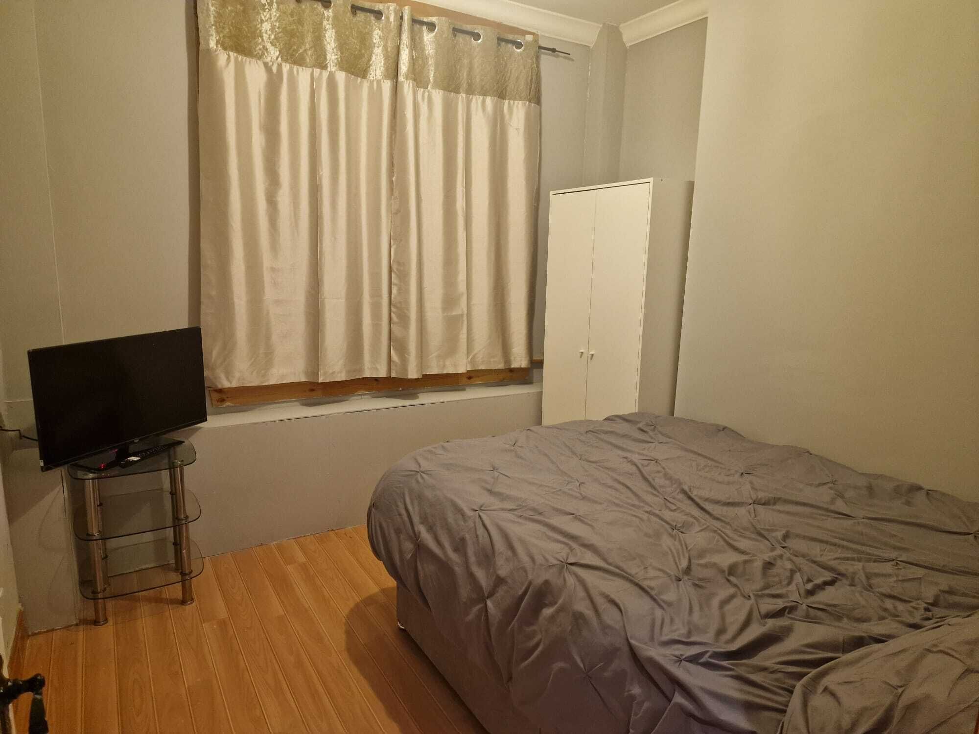 Een slaapkamer met een bed, een televisie op een tafeltje, een kast en een raam met gordijnen.