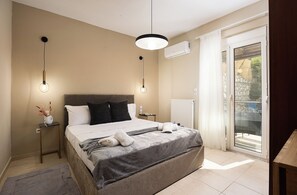A bedroom with a large bed, two bedside tables, a nightstand, a ceiling light, an air conditioning unit, and a sliding glass door to the outside.