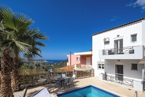 A two-story building with a pool, outdoor furniture, and a view of the sea.