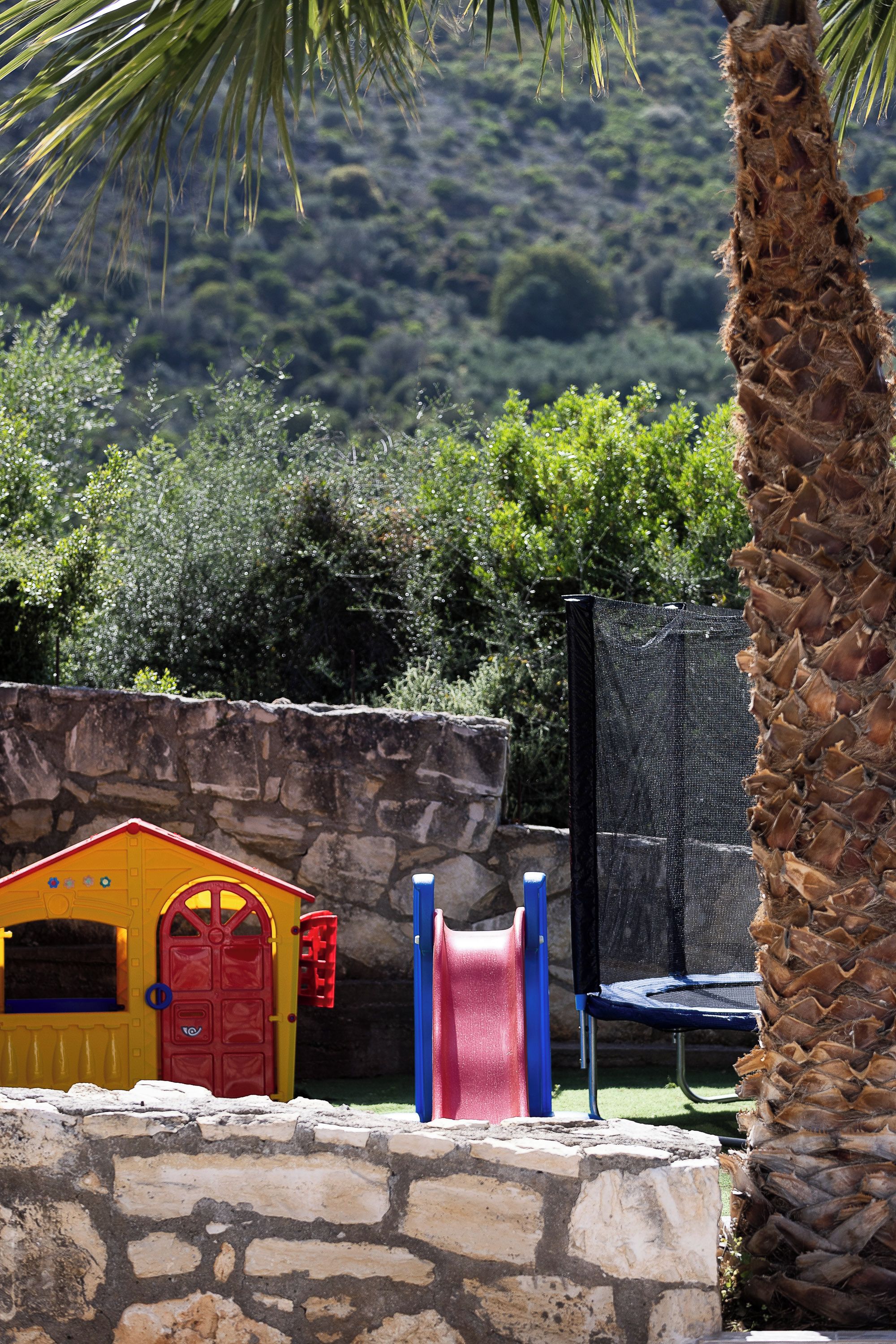Un espace de jeux pour enfants avec une petite maison de jeu jaune, un toboggan rouge et un trampoline.