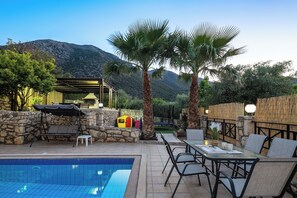 A poolside area with a table and chairs, a small play structure, and a stone wall.