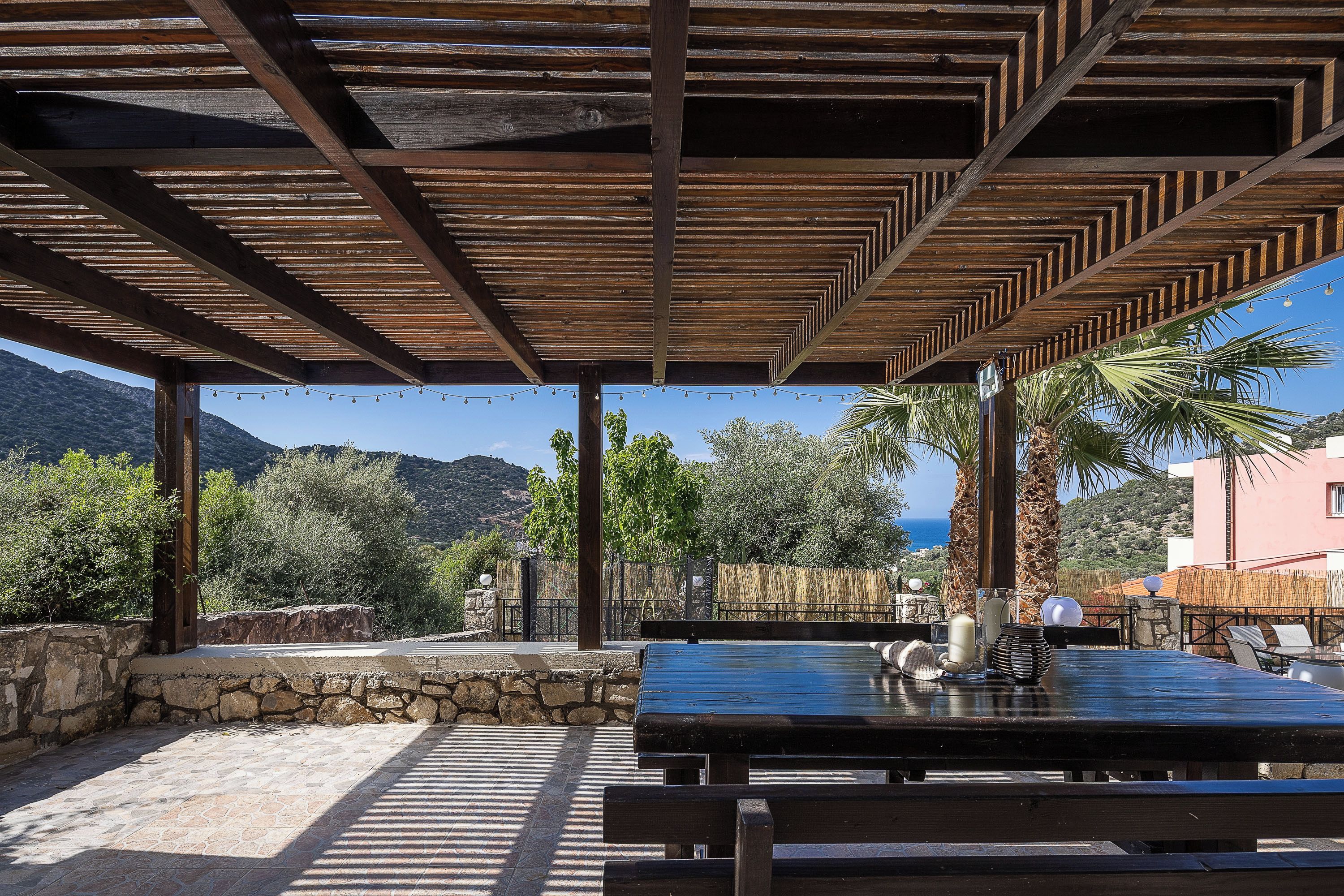 Eine Terrasse im Freien mit einer Holz-Pergola, Steinmauern und einem Tisch mit Stühlen.