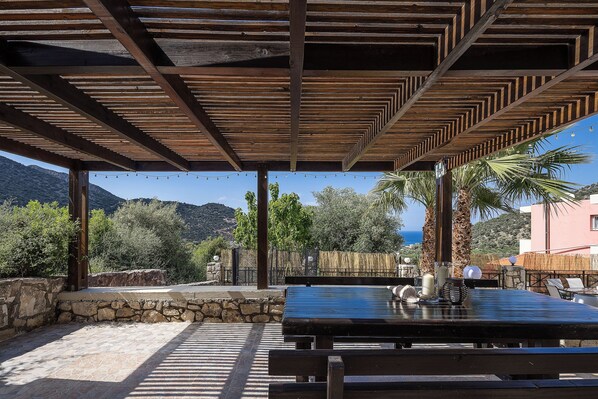 An outdoor patio with a wooden pergola, stone walls, and a table with chairs.