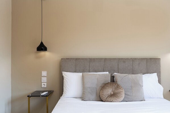 A neatly arranged bedroom with a bed, pillows, a bedside table, and a hanging light fixture.