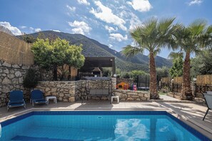 A swimming pool with a stone wall and a covered seating area.