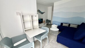 A compact living space with a white desk, two green chairs, a blue sofa, and a small round table. - 33 AN - Stay Napa Ocean Apartment (Ayia Napa)