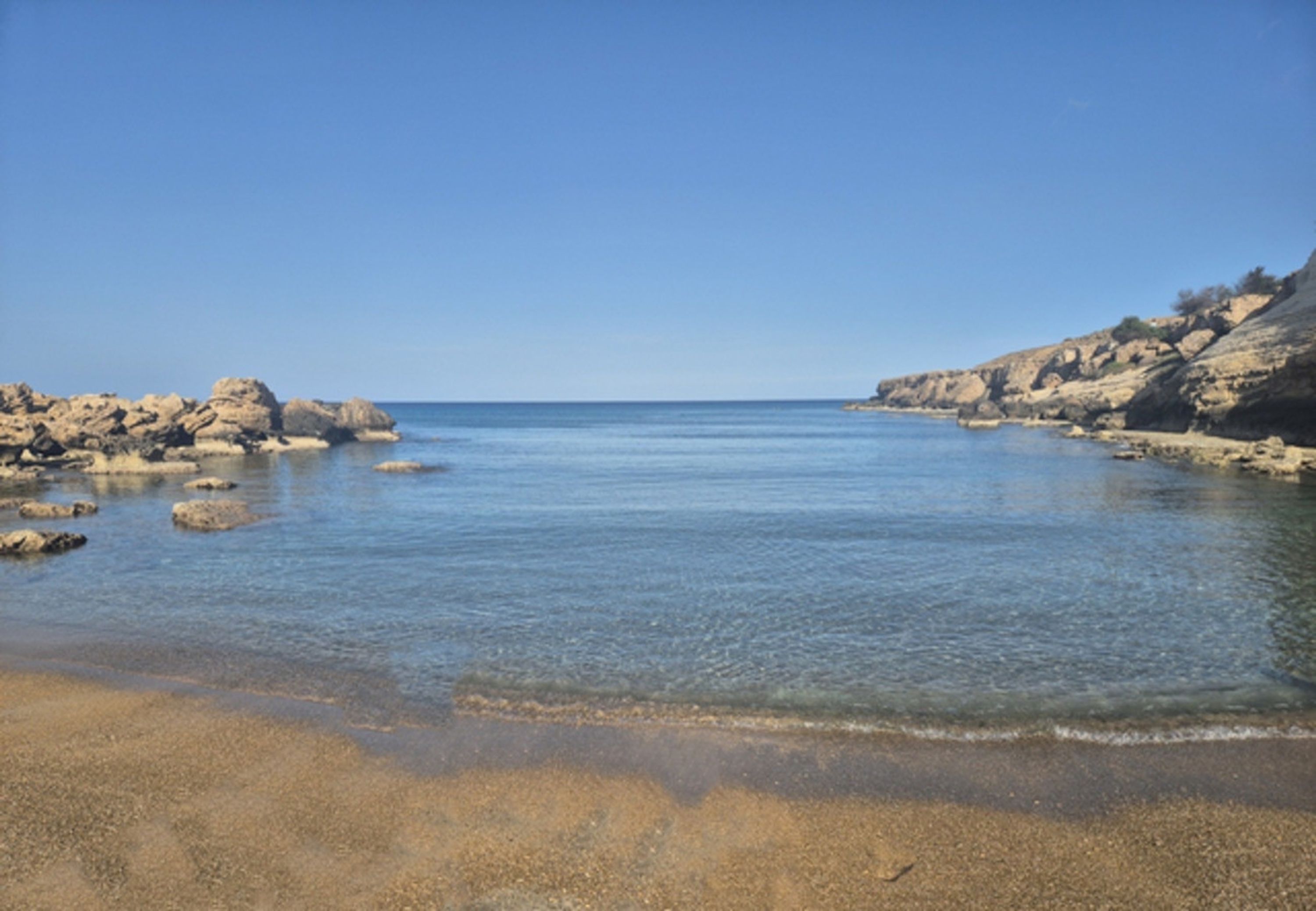 Une plage côtière avec une eau claire, des formations rocheuses et un rivage sablonneux.