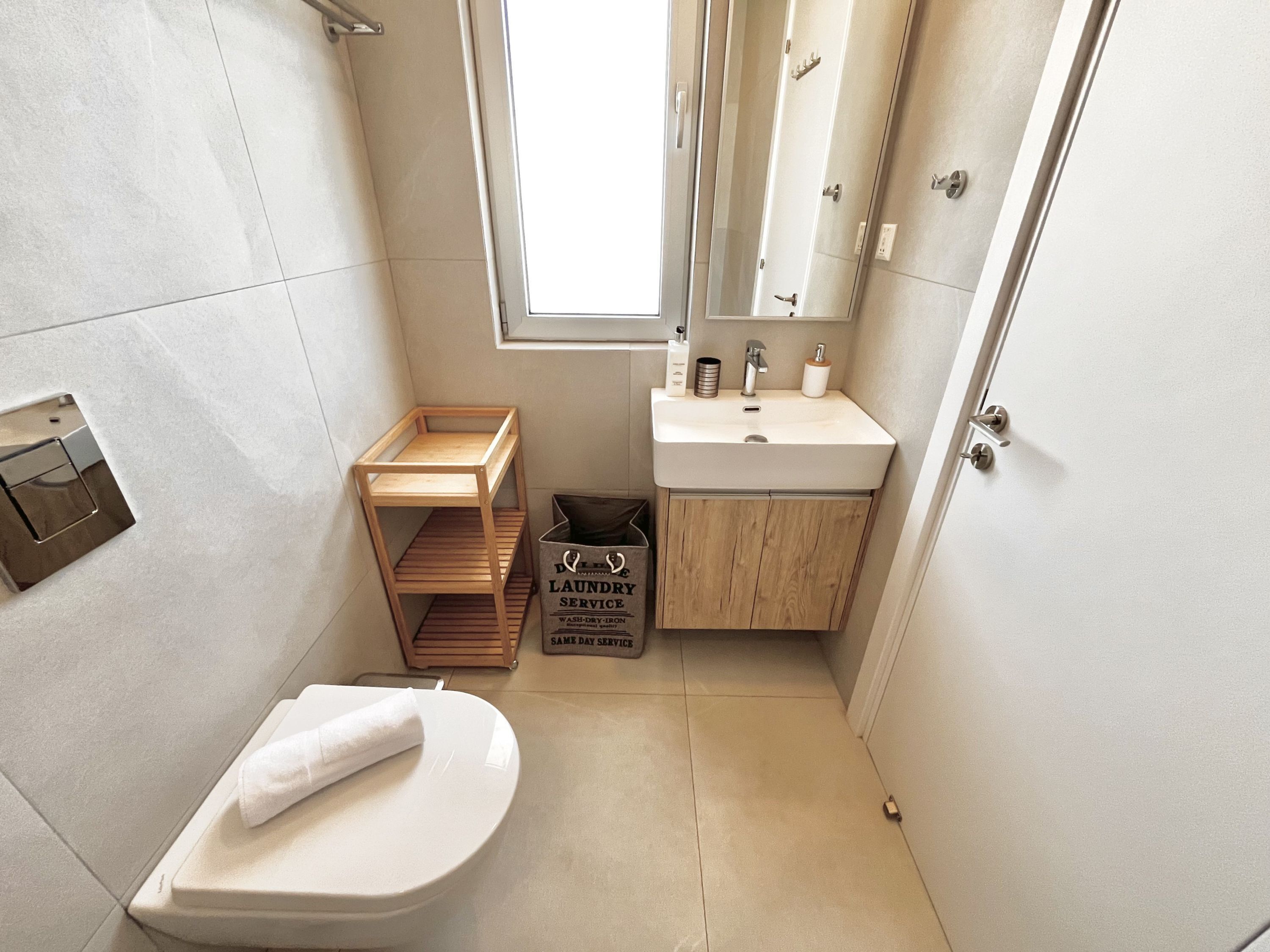 Une petite salle de bain comprenant des toilettes, un lavabo, un miroir et une petite étagère en bois.