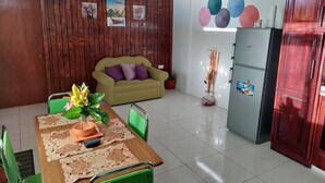 Un coin repas avec une table en bois, des chaises vertes, un canapé et un réfrigérateur.