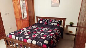 Une chambre à coucher avec un cadre de lit en bois, une couvre-lit à motifs, une petite table de chevet avec une plante et une étagère fixée au mur.