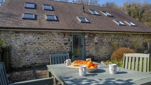 A stone building with a sloped roof, a door, and a table with a bowl of oranges and two mugs. - Bluebell Cottage, Aberporth (Aberporth)