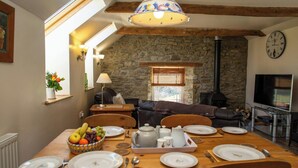 A cozy dining area with a stone wall, wooden beams, a fireplace, and a television. - Bluebell Cottage, Aberporth (Aberporth)