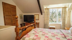 Un dormitorio con cama de madera, televisor, ventana con cortinas y vistas a árboles desde el exterior.
