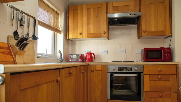 Una cocina con armarios de madera, una campana extractora de acero inoxidable, un hervidor rojo, un tostador y un horno empotrado.
