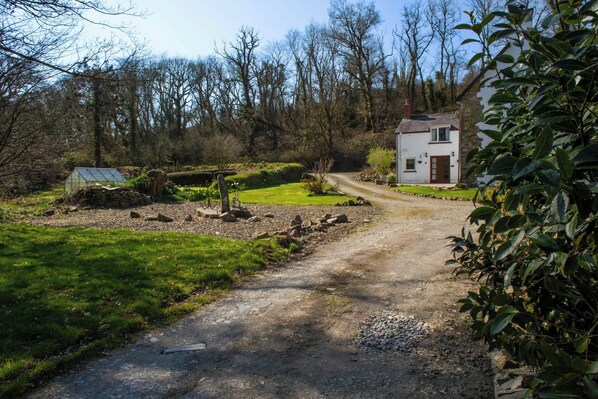 A rural pathway leading to a stone house with a white facade and a red door.
