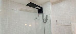 A glass-enclosed shower with white tiled walls and a black showerhead. - COCAZ0101 - Smart Costa Azul (Salvador)
