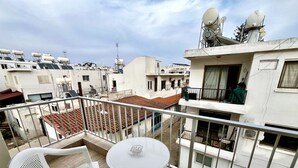 A balcony with white plastic chairs and a small round table, overlooking a residential area with tiled roofs and satellite dishes. - 101 AN -chill n Joy Apartment (Ayia Napa)