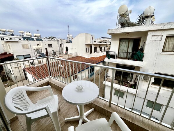 A balcony with white plastic chairs and a small round table, overlooking a residential area with tiled roofs and satellite dishes. - 101 AN -chill n Joy Apartment (Ayia Napa)