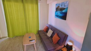 A room with a sofa, a small table, a lamp, and a painting on the wall. - 101 AN -chill n Joy Apartment (Ayia Napa)