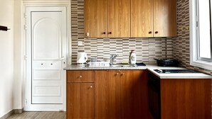 A kitchen with wooden cabinets, a white door, a tiled backsplash, and a stove. - 101 AN -chill n Joy Apartment (Ayia Napa)