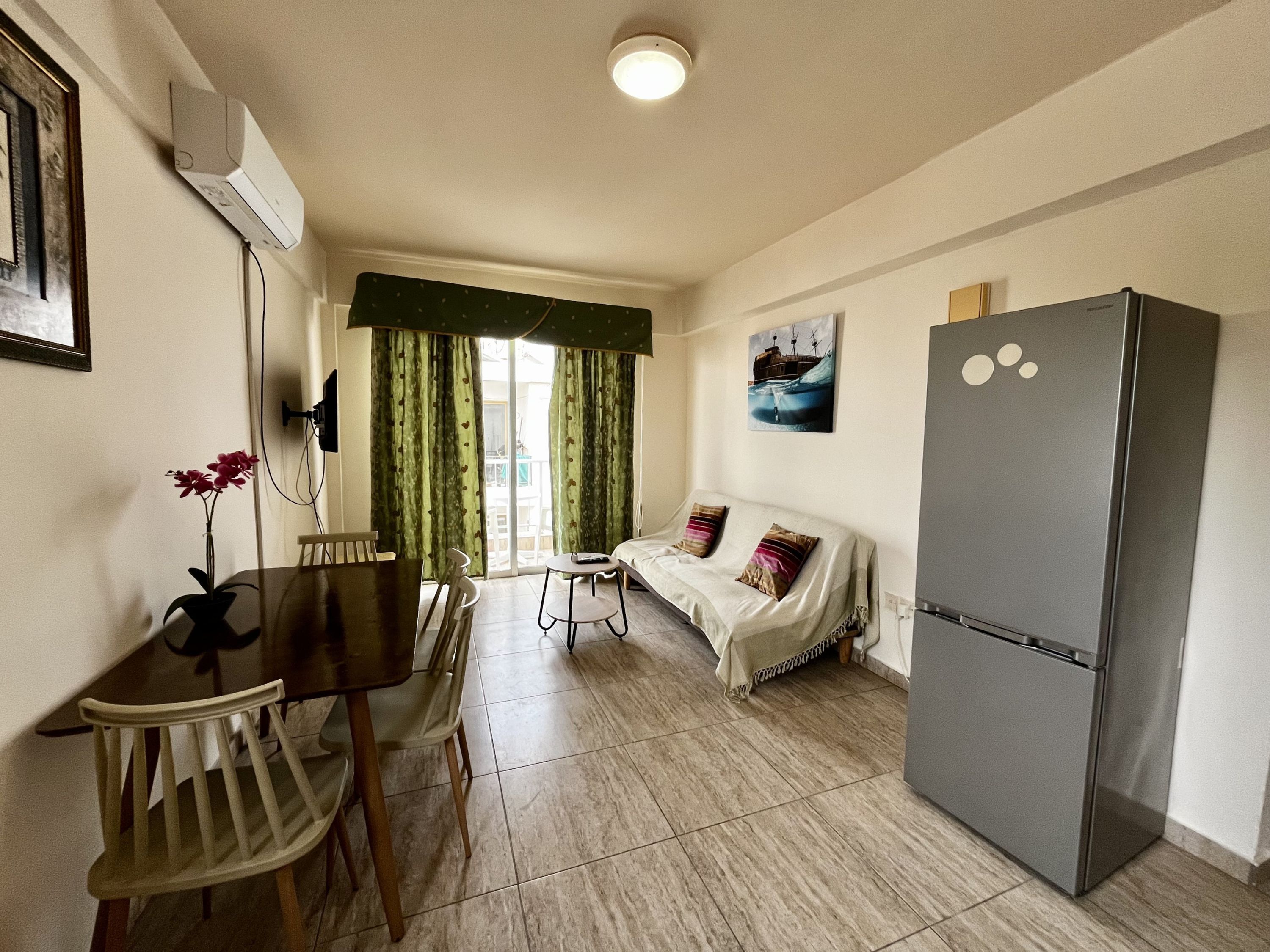 Un espacio habitable compacto con comedor, sofá, refrigerador y ventana con cortinas.