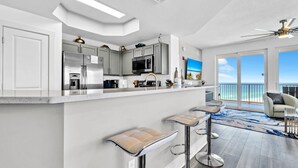 Una cocina moderna con electrodomésticos de acero inoxidable, una barra con taburetes y vista al océano a través de amplias puertas correderas.