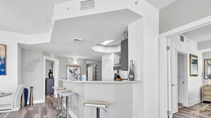 Una cocina moderna con armarios blancos, una isla central con taburetes y vistas al comedor contiguo.