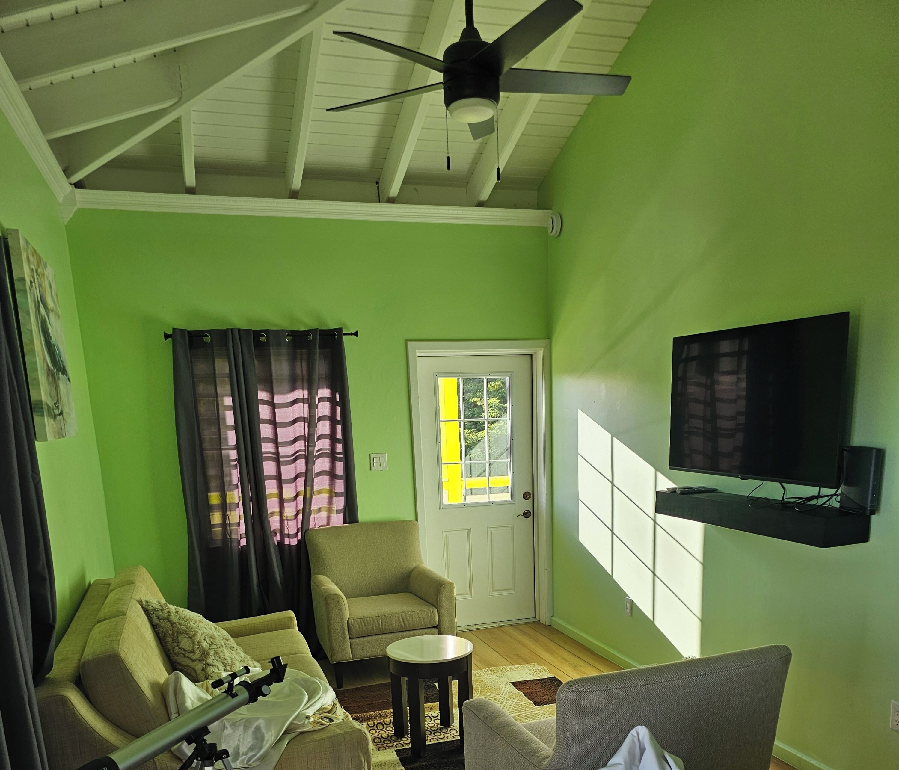 A living room with a ceiling fan, a television mounted on the wall, a sofa, a chair, and a small table.