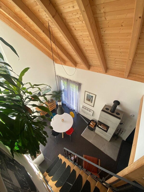 Una sala de estar moderna con techo de madera, comedor con mesa redonda y estufa de leña empotrada.
