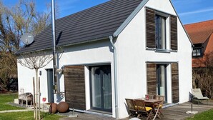 A modern two-story house with a sloped roof, large sliding glass doors, and a deck with outdoor furniture. - Vacation home Annemie - very cozy and modern house with a beautiful garden (Markt Erlbach)