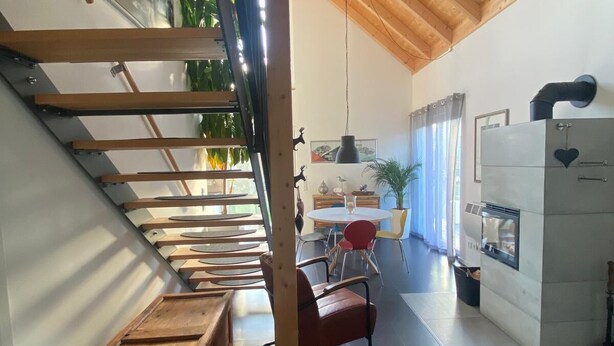 A modern interior with a wooden staircase, a dining area with red chairs, and a kitchen with a built-in oven. - Vacation home Annemie - very cozy and modern house with a beautiful garden (Markt Erlbach)